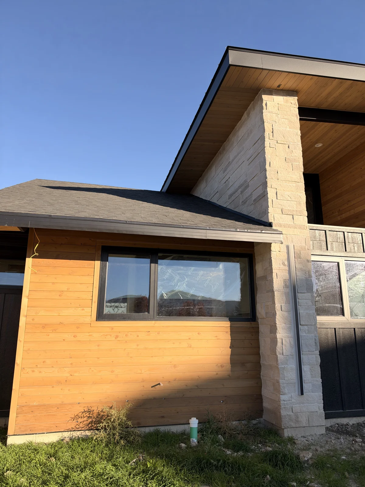 Close-up of a shingle roof, dark fascia, cedar soffit, and stone exterior